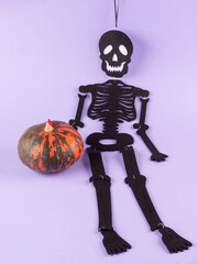 Black halloween skeleton with orange pumpkin on purple background