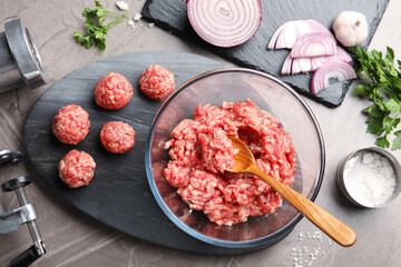 Raw meatballs, ground meat, parsley, onion and grinder on grey table, flat lay