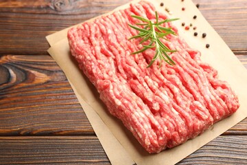 Raw minced meat with peppercorns and rosemary on wooden table, closeup. Space for text