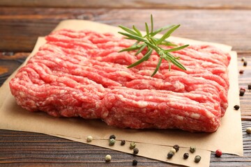 Raw minced meat with peppercorns and rosemary on wooden table, closeup