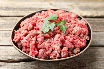 Fresh raw minced meat with parsley in bowl on wooden table, closeup