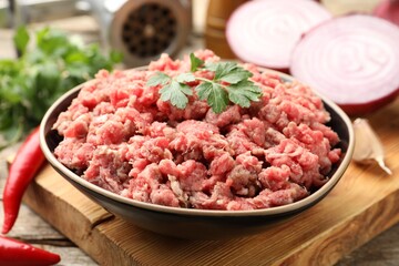 Raw minced meat with parsley in bowl on wooden table, closeup