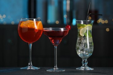 Glasses of tasty cocktails on dark table against blurred background, bokeh effect