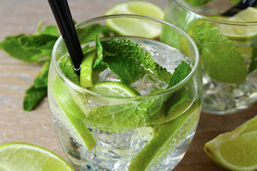 Glasses of tasty cocktails with lime and mint on wooden table, closeup