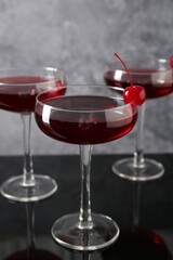 Glasses of tasty cocktails with garnish on mirror surface, closeup