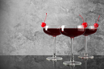 Glasses of tasty cocktails with garnish on mirror surface, space for text