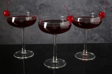 Glasses of tasty cocktails with garnish on mirror surface, closeup