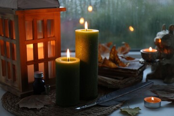 Burning candles, lantern, vintage books, ink and quill on windowsill on rainy day. Autumn atmosphere