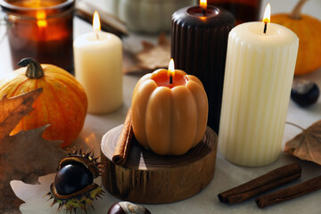 Different burning candles and autumn decor on white table indoors, closeup