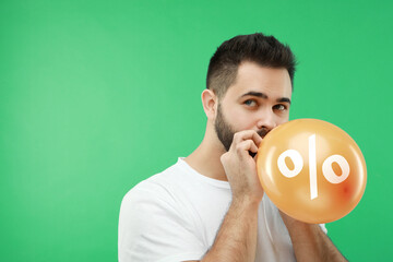 Man blowing orange balloon with percent sign on green background. Discount offer