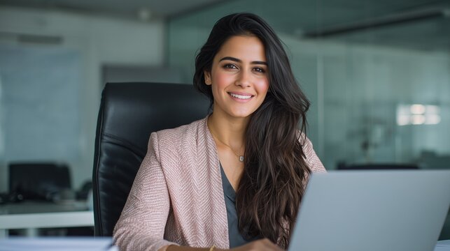 Portrait young it specialist latin hispanic business lady working on laptop pc sitting at desk in modern office smiling at camera. Middle eastern indian woman using computer technology for work online