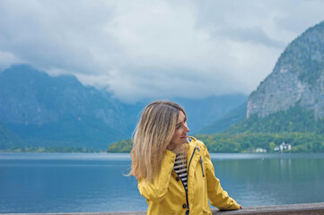 Fototapeta premium Woman in Yellow Jacket Admiring Hallstatt Lake, Austria. Travel and Tourism Concept in Scenic Alpine Village