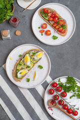 Open sandwiches with meat, egg, and vegetables on light-colored plates on a gray table
