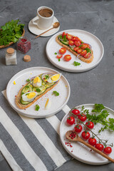 Open sandwiches with meat, egg, and vegetables on light-colored plates on a gray table