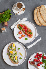Open sandwiches with meat, egg, and vegetables on light-colored plates on a gray table