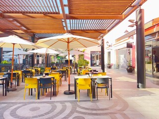 Sunny open-air café terrace with yellow chairs and white umbrellas on a modern promenade