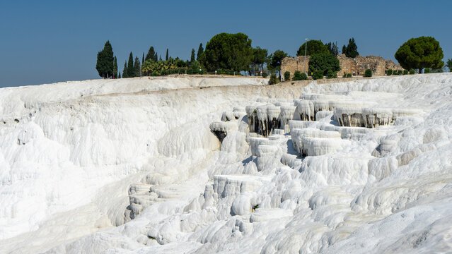Beautiful white carbonate mineral plateau or travertine terraces in Pamukkale or cotton castle, Denizli Province, Turkey. Walls of Hierapolis, Hellenistic Greek city. Unesco world heritage site.