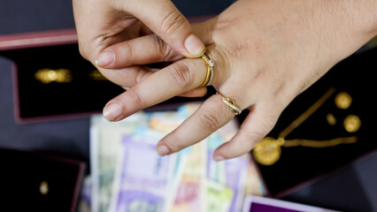 Female Hand Trying On Precious Gold Jewelry At Home Over blurred Indian Currency background