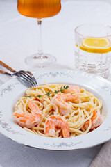Pasta with shrimp and thyme, served on a white plate, with a glass of white wine, the table is set, there are no people,