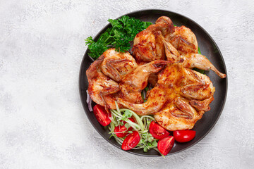 Baked quail, served on a plate with crispy lettuce leaves, fresh tomatoes and herbs, on a dark plate, homemade,