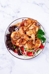 Baked quail, served on a plate with crispy lettuce leaves, fresh tomatoes and herbs, on a white plate, homemade,