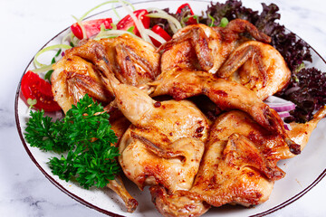 Baked quail, served on a plate with crispy lettuce leaves, fresh tomatoes and herbs, on a white plate, homemade,