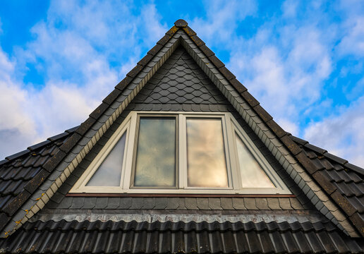 Roof gable with attic dormer window against blue sky