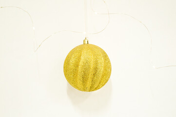 Single Shiny Gold Glitter Christmas Bauble Hanging on a Thin Wire Against a White Background. Isolated
