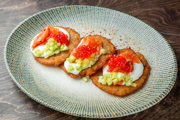 Gourmet potato pancakes topped with sour cream, smoked salmon, red caviar, and cucumber on a rustic plate. Elegant appetizer or brunch dish with vibrant colors and refined presentation.