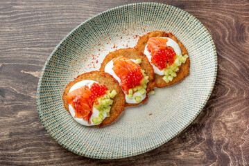 Gourmet potato pancakes topped with sour cream, smoked salmon, red caviar, and cucumber on a rustic plate. Elegant appetizer or brunch dish with vibrant colors and refined presentation.