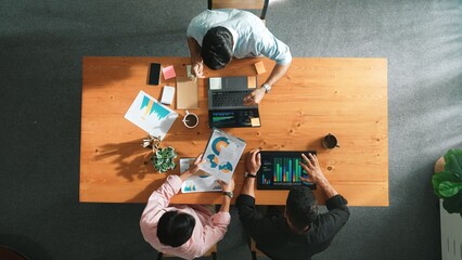 Top view of business team working together while manager join meeting and using laptop to analyze financial chart. Group of attractive people sharing idea and solving problem together. Convocation.