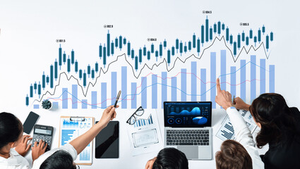 A diverse business team collaborates to analyze financial graphs and market data, utilizing technology and documents in a professional workspace. Scalp