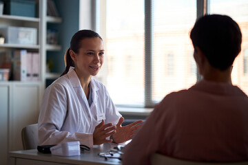 Caucasian young adult female doctor explaining diagnosis to young adult female patient during medical consultation in clinic office, discussing cancer treatment options and support