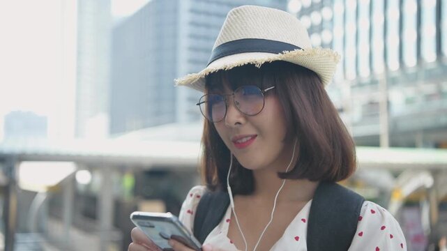 Travel concept of 4k Resolution. Asian woman listening to music with mobile phone in city.