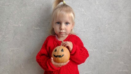 A little girl holds a pumpkin on Halloween, preparing for the celebration