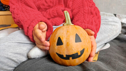 A little girl holds a pumpkin on Halloween, preparing for the celebration