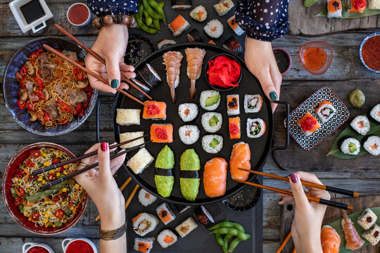 Japanese sushi rolls like Philadelphia roll, dragon roll and California roll with salmon, crab and calamari, Unrecognizable people enjoying a sushi meal with chopsticks