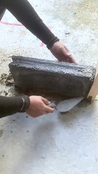 Construction worker laying concrete blocks with cement mortar at building site. Close-up of hands during masonry work under sunlight, showing texture and building process.