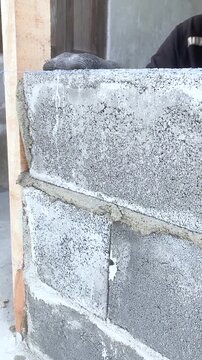 Construction worker laying concrete blocks with cement mortar at building site. Close-up of hands during masonry work under sunlight, showing texture and building process.