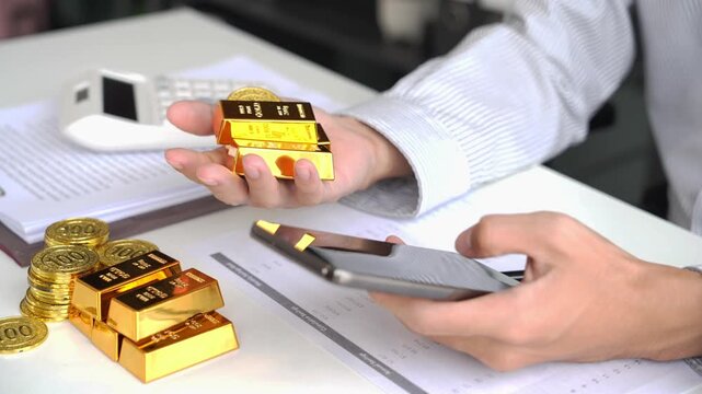 Gold Trading Businessman invest in trading gold, calculating profit price of gold in stock market when price rising rapidly, using phone monitoring gold price in stock market.