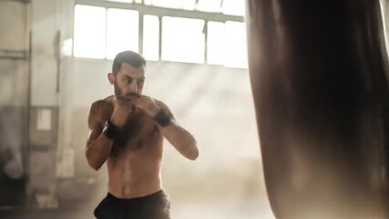 Muscular man with beard boxing with a punching bag in a gym, intense workout session