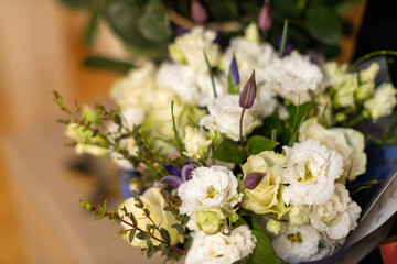 A vibrant bouquet features a mix of white and light yellow flowers with green foliage and hints of purple buds, creating a soft and elegant display.