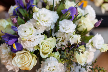 A vibrant bouquet features white roses, ruffled white eustoma, and striking purple irises with green foliage.