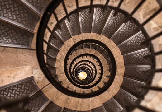 Capturing a mesmerizing view from above, a spiral staircase descends with elegant metal handrails and beige stone steps, creating a hypnotic pattern that draws the eye - Powered by Adobe