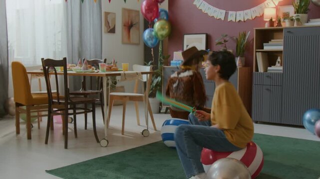Two happy boys on bouncing balls enjoying birthday celebration in festively decorated with banners and balloons room