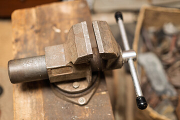 A close-up shot of a rusty, old metal workbench vise with its jaws slightly open on a wooden surface in a workshop.
