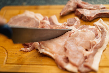 A close-up view captures a hand slicing fresh pork with a sharp knife on a wooden cutting board, showcasing culinary preparation.