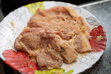 Raw meat pieces are coated with a breading mixture and arranged on a decorative plate, ready for cooking.