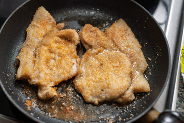 Breaded cutlets are sizzling in a hot pan, cooking to a golden brown perfection.
