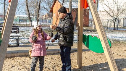 Grandfather playing with his granddaughter on the playground in the park in winter
